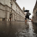LONDON - JANUARY 23: A woman steps over a rain splashed puddle infront of the Treasury building (L) on January 23, 2009 in London. Statistics released today show that the United Kingdom is officially in recession after two successive quarters of negative growth were recorded in 2008. (Photo by Peter Macdiarmid/Getty Images)