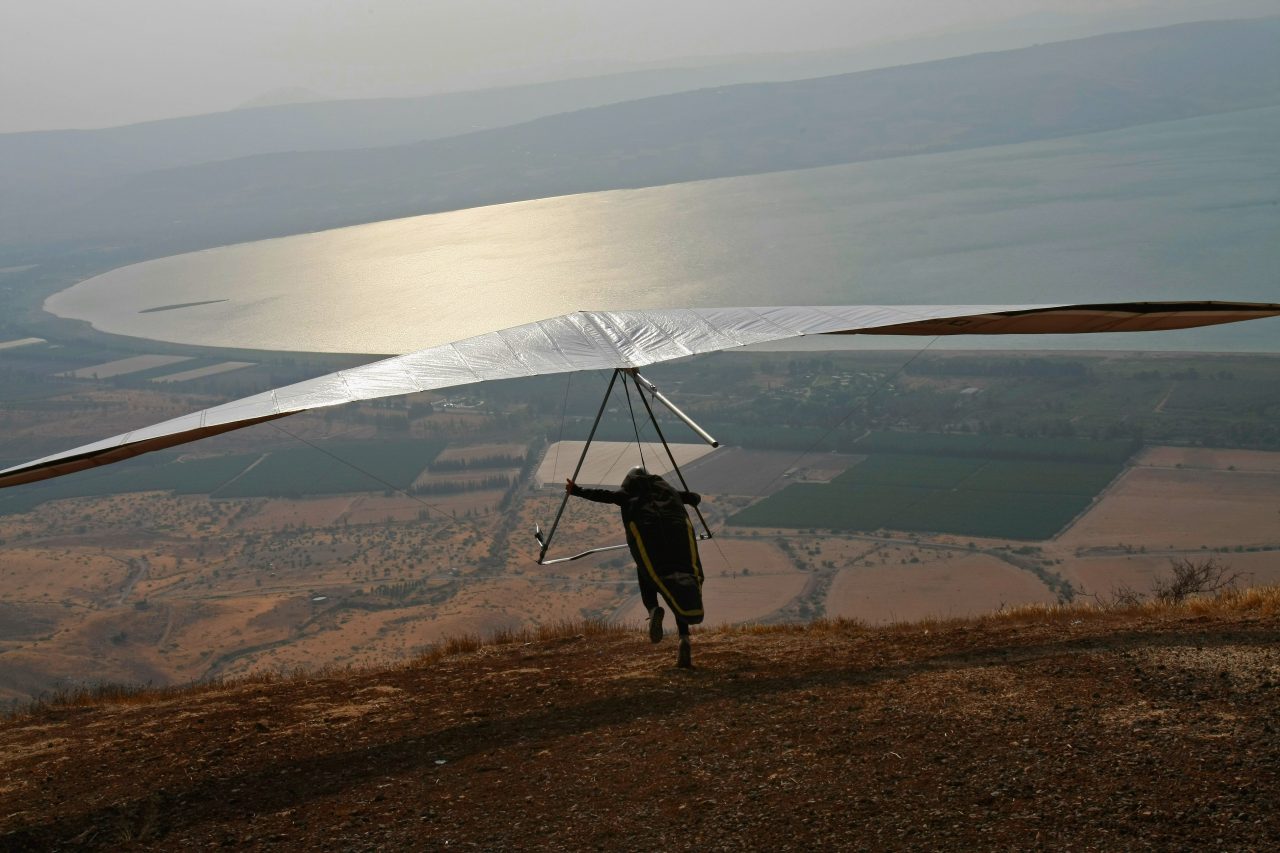 MEVO HAMA, GOLAN HEIGHTS - AUGUST 28: An Israeli hangglider launches himself from the cliffs looming over the Sea of Galilee to catch the thermals rising from the water during the Holy Wind festival on August 28, 2008 on the Mevo Hama cliffs on the Golan Heights. The biblical lake is Israel's most important water reservoir, fed by the Jordan River from the north and by the many streams that carry snow melt and rain water from the strategic Golan Heights. Jerusalem may soon find itself surrendering the volcanic plateau to Syria, with Damascus demanding a full Israeli withdrawal from the Golan in return for a comprehensive peace. (Photo by David Silverman/Getty Images)